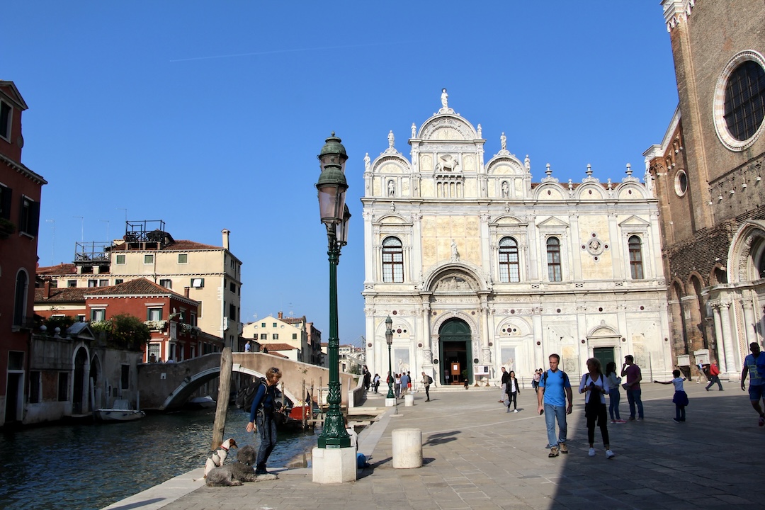 Une place ensoleillée à Venise avec des églises et des touristes qui se promènent.