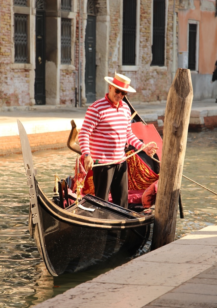 Un gondolier à Venise en tenue traditionnelle avec chapeau en paille et polo rayé rouge.