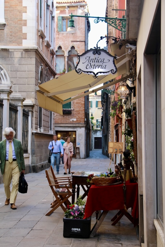 Une petite ruelle calme avec une terrasse d'osteria et des vénitiens bien habillés qui passent devant.